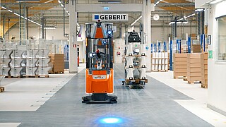 Geberit üretim sahasında mavi emniyet ışığıyla otonom malzeme taşıyan STILL EXV iGo AGV filosu